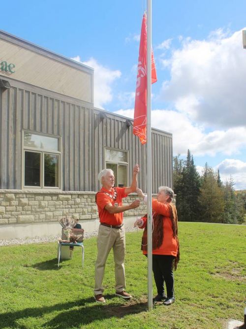 Shabot Obaadjiwan Chief Doreen Davis and North Frontenac Mayor Ron Higgins jointly raise the orange Every Child Matters Flag at the municipal office in Plevna during a ceremony Sept. 30. “It will fly alone today and tomorrow we shall raise the Township Flag with this flag at half mast,” said Higgins. “It shall fly at half mast until every child that is anonymously buried is brought home.” Photo/Craig Bakay